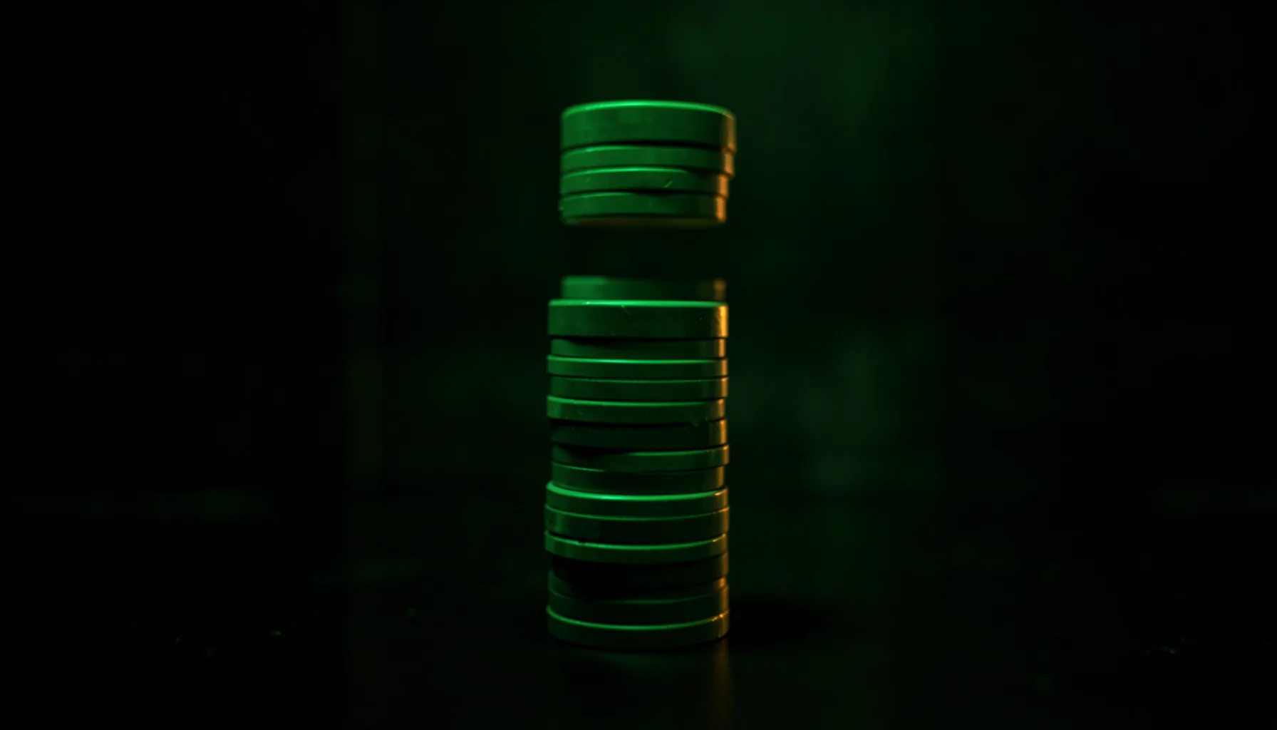 Dark atmospheric photograph of stacked casino chips in soft green and amber lighting